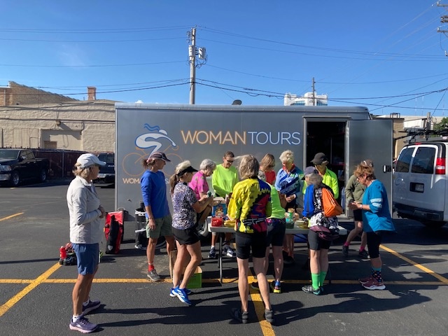 Picture shows a group of women in cycling shorts gathering around a table that is in front of a trailer. 