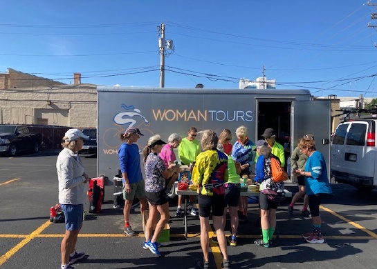 Picture shows a group of women in cycling shorts gathering around a table that is in front of a trailer. 