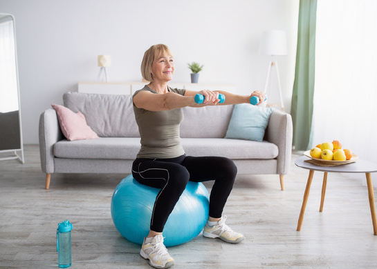 Woman is exercising in her living room with dumbbells and stability ball. 