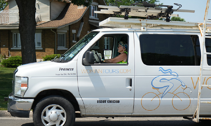 Photo shows a woman driving a white WomanTours van that is labeled with the name Frances. 