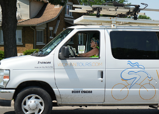 Photo shows a woman driving a white WomanTours van that is labeled with the name Frances. 